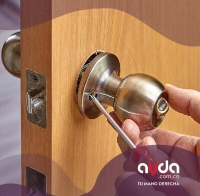 Persona instalando una chapa de puerta con destornillador en una puerta de madera.